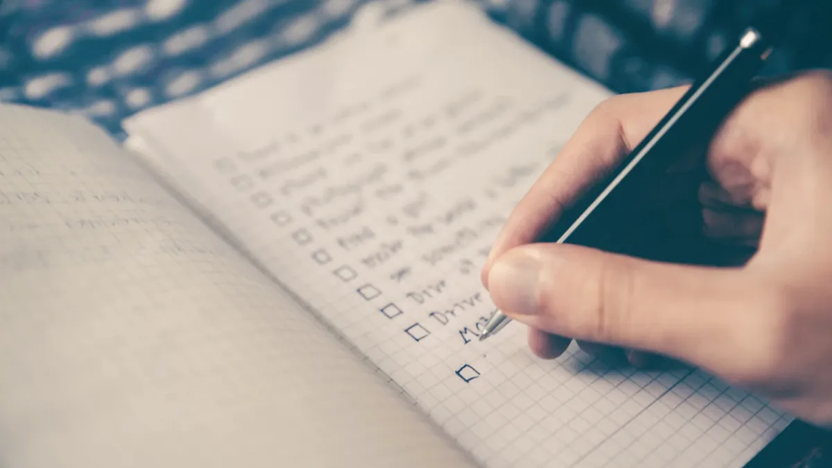 Eine Hand schreibt eine Checkliste in ein Notizbuch