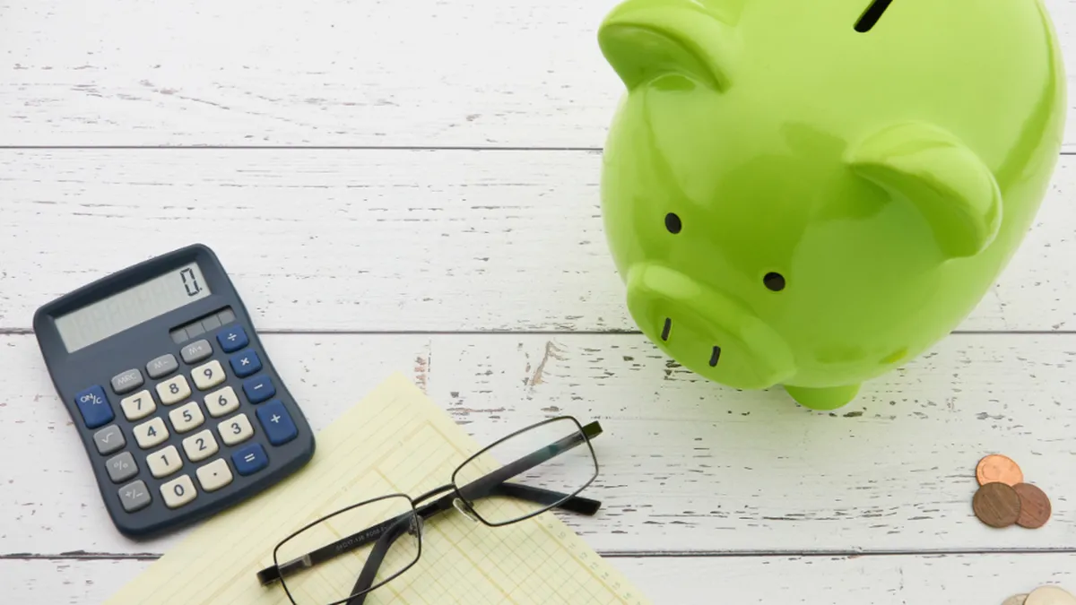 A piggy bank, calculator, and notepad on a desk